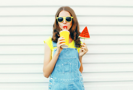 Fashion portrait pretty cool girl drinks a juice from cup holds slice watermelon ice cream over a white の写真素材