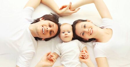 Closeup portrait happy family, father, mother and baby together lying on the bed at home, top view