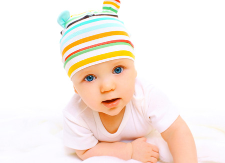Portrait closeup of baby in colorful hat crawls on a white backgroundの写真素材