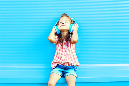 Happy little girl child listens to music in headphones on a colorful blue backgroundの写真素材