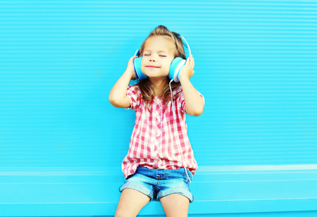little girl child listens to music in headphones on a colorful blue backgroundの写真素材