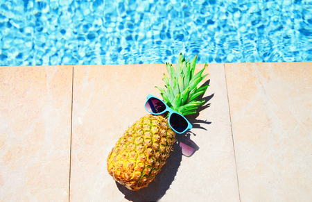 Fashion pineapple with sunglasses, blue water pool background, summer holidays, vacation, food conceptの写真素材