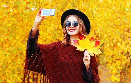 Autumn fashion smiling young woman taking a picture self portrait on the smartphone in knitted ponchoの写真素材