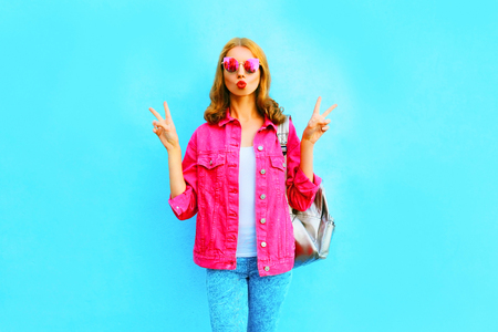 Fashion pretty woman make an air kiss wearing pink denim jacket on blue background