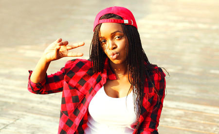 Cool girl sitting is having fun in the city, wearing a red checkered shirt and baseball cap