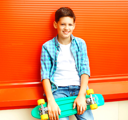 Fashion smiling teenager boy with skateboard in a checkered shirt on orange backgroundの写真素材