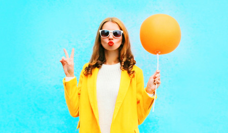 Fashion portrait woman holds orange air balloon in yellow coat on colorful blue backgroundの写真素材
