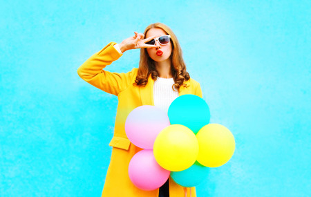 Fashion woman with an air balloons in a yellow coat on colorful blue backgroundの写真素材