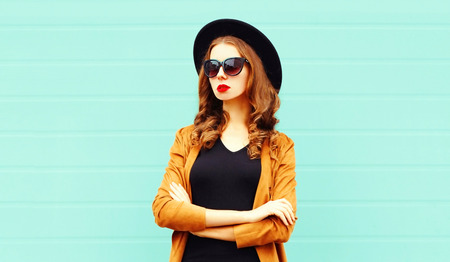 Fashion portrait young woman in black round hat, sunglasses posing on gray wall backgroundの写真素材