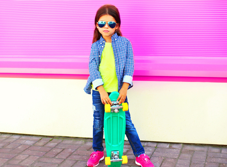 Fashion child little girl holds skateboard on pink wall backgroundの写真素材