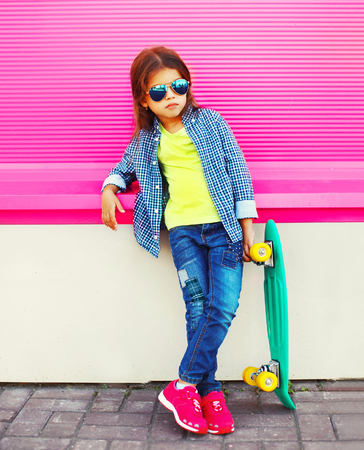 Fashion child little girl with skateboard on pink wall backgroundの写真素材