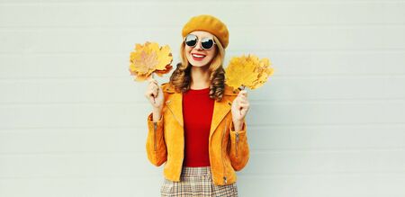 Autumn season! Stylish happy smiling woman with yellow maple leaves in french beret posing over gray wall backgroundの写真素材
