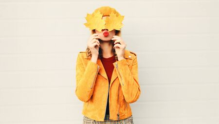 Autumn mood! woman holding in her hands yellow maple leaves hiding her eyes over gray wall...