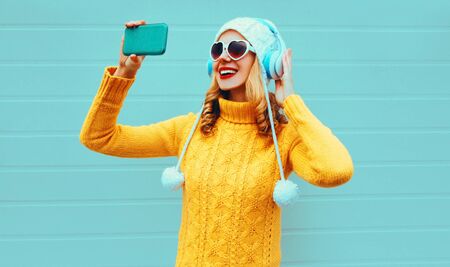Winter portrait smiling woman taking selfie picture by phone while listening to music in wireless...