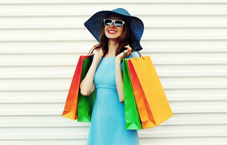 Portrait happy smiling woman with shopping bags wearing blue dress, summer straw round hat and...