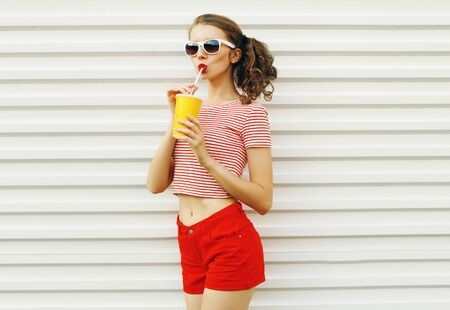Summer portrait attractive young woman drinking juice on white wall backgroundの写真素材