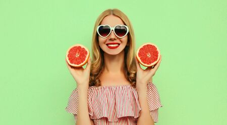 Summer portrait of smiling young woman showing juicy grapefruit over green backgroundの写真素材