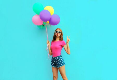 Attractive young woman with bunch of colorful balloons having fun on blue wall background