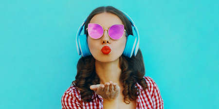 Portrait of attractive young woman in wireless headphones listening to music blowing red lips...