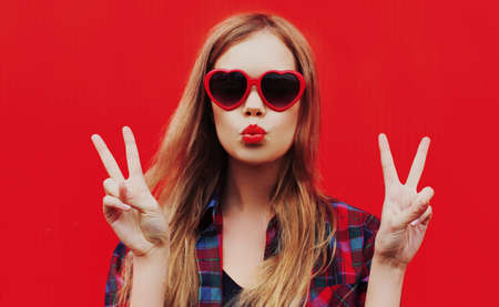 Close up of young woman blowing red lips sending sweet air kiss wearing a red heart shaped...