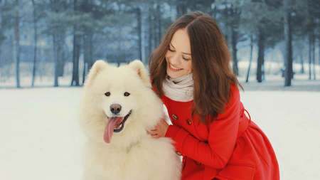 Portrait of beautiful smiling young woman owner with white Samoyed dog in winter parkの写真素材