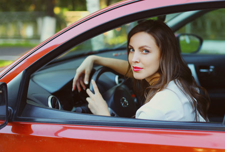 Portrait of beautiful young woman driver behind a wheel red carの写真素材
