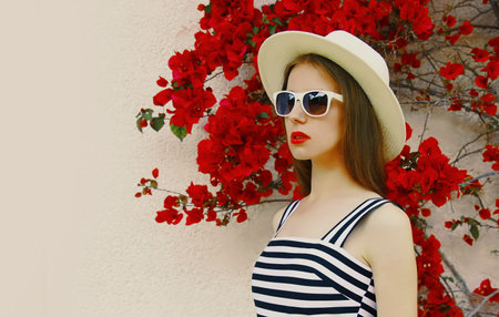 Portrait of beautiful woman wearing a summer straw hat on a red flowers background