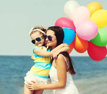 Happy mother and little girl child with colorful balloons on a beach over a sea backgroundの写真素材