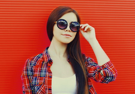 Portrait of beautiful young brunette woman wearing a sunglasses in a city on red backgroundの写真素材