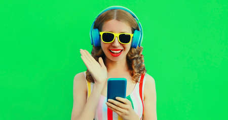 Summer colorful portrait of happy smiling young woman listening to music in headphones with phone on...