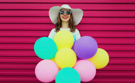 Portrait of beautiful happy smiling young woman with bunch of balloons wearing a colorful dress on pink backgroundの写真素材