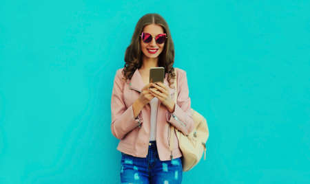 Portrait of smiling young woman with smartphone on blue backgroundの写真素材