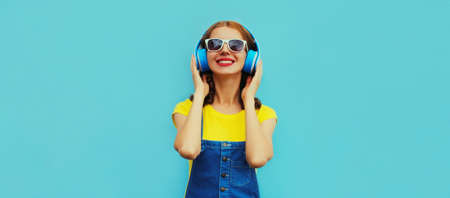 Portrait of happy smiling young woman with headphones listening to music on a colorful blue...
