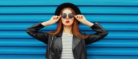 Portrait of stylish woman posing wearing a black round hat on blue backgroundの写真素材