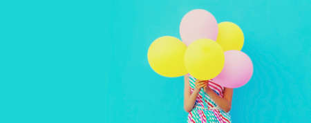Woman covering her head with bunch of colorful balloons on a blue backgroundの写真素材