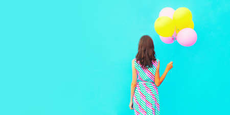 Rear view woman with bunch of colorful balloons on a blue background