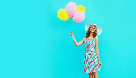 Portrait of beautiful happy smiling young woman with bunch of balloons wearing a colorful dress on blue backgroundの写真素材