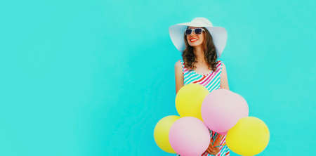 Portrait of beautiful happy smiling young woman with bunch of balloons wearing a colorful dress on...