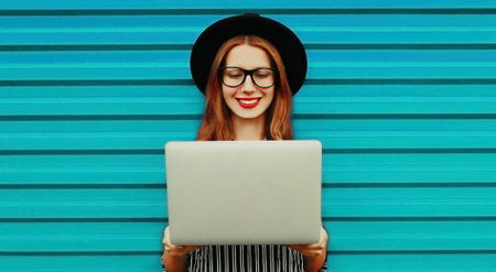 Portrait of happy smiling young woman working with laptop on colorful blue backgroundの写真素材