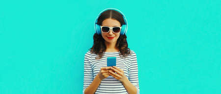 Portrait of smiling young woman in headphones listening to music with smartphone on blue backgroundの写真素材