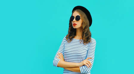 Portrait of stylish young woman model posing wearing a striped t-shirt and summer straw round hat on blue backgroundの写真素材
