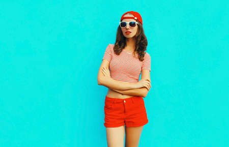 Summer portrait of young woman wearing baseball cap, red shorts on blue backgroundの写真素材