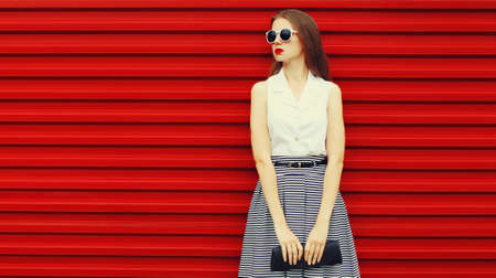 Portrait of stylish young woman model posing wearing skirt, handbag on red backgroundの写真素材