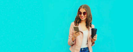 Portrait of beautiful smiling young woman looking at smartphone on blue background, blank copy space