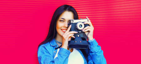 Portrait of young woman photographer with vintage film camera on pink backgroundの写真素材