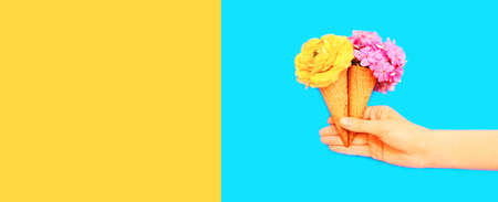 Hand holding cone ice cream with flowers on blue background, blank copy space for advertising text