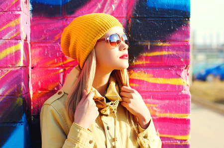 Fashion portrait of beautiful stylish blonde young woman on city street over colorful graffiti...
