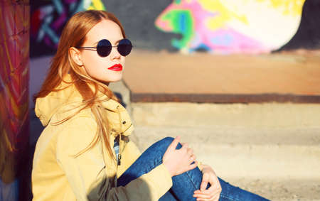 Fashion portrait of beautiful stylish blonde young woman on city street over colorful graffiti backgroundの写真素材