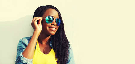 Portrait of happy smiling young african woman model wearing sunglasses, colorful clothes on white background, blank copy space for advertising textの写真素材