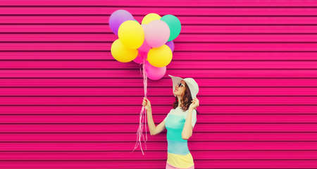 Portrait of beautiful happy smiling young woman with bunch of balloons wearing a colorful dress on...